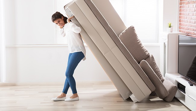 Smiling Young Woman Trying To Move Large Sofa At Home | Dehart Tile