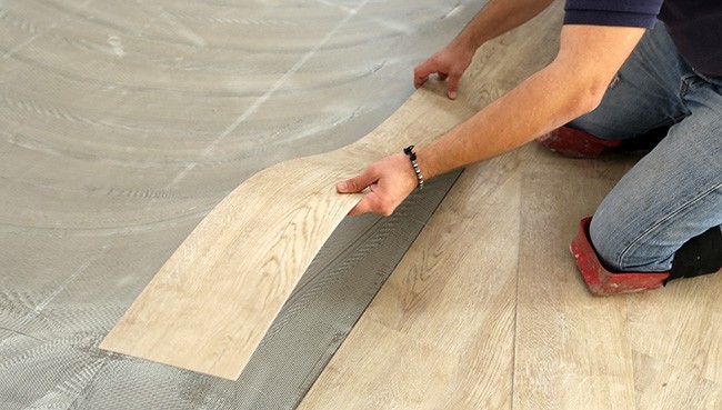Worker installing new vinyl tile floor | Dehart Tile