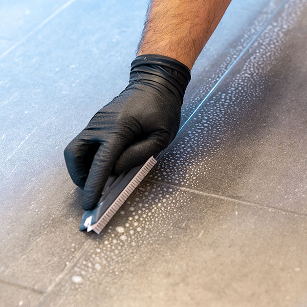 Professional cleaner cleaning grout with a brush blade | Dehart Tile